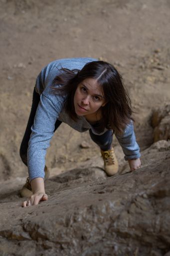 young girl learning rock climbing in high mountain with blue sweater, black tights and boots.