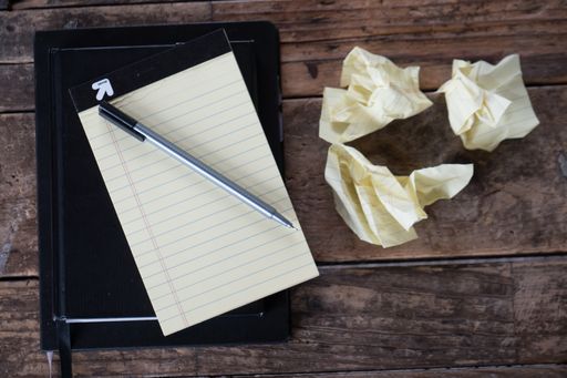 An overhead shot of a pen with a textbook next to crumpled pieces of paper on a wooden surface