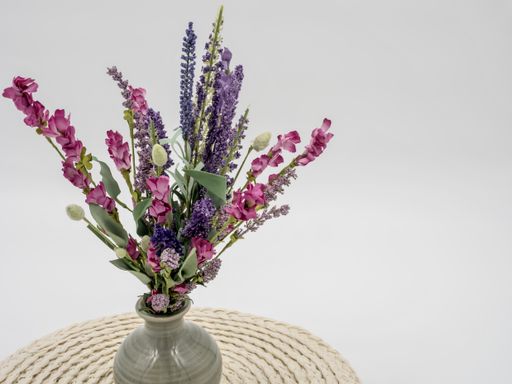 A high angle shot of multicolor flowers in a  vase on a straw tray  against a grey background