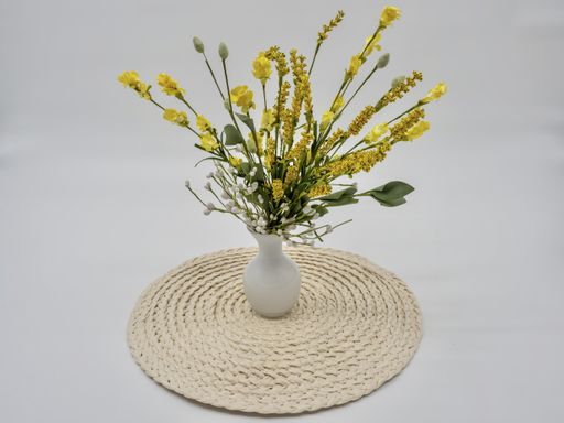 A picture of yellow flowers in a white vase on a straw tray  against a grey background
