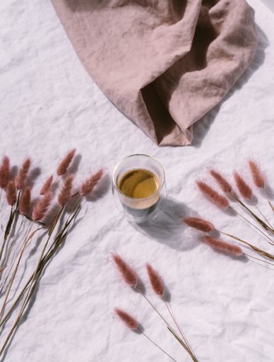 A glass of coffee next to dry red plants and a light brown piece of burlap
