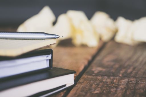 A closeup shot of textbooks with a gray pen and crumpled pieces of paper around on a wooden surface