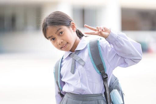 A portrait of Southeast Asian pupil with school uniform making the sign of victory with fingers.