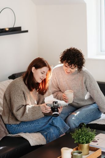 A vertical shot of two females, a curly female taking a coffee cup, a redhead lady holding a camera