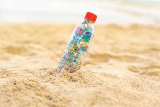 A selective focus of a plastic bottle filled with microplastics in the sandy beach