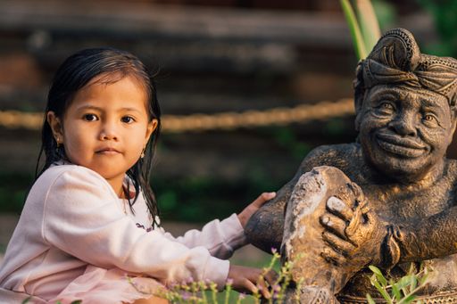 A closeup shot of an adorable female child near a statue in Bali, Indonesia