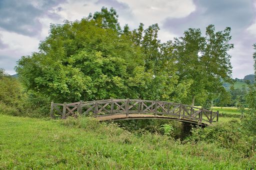 A small wooden bridge in a field under the cloudy sky