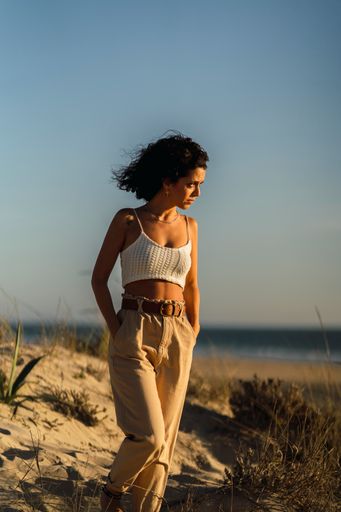 A vertical shot of a sexy young female with curly hair and a small tattoo posing on a sunny beach