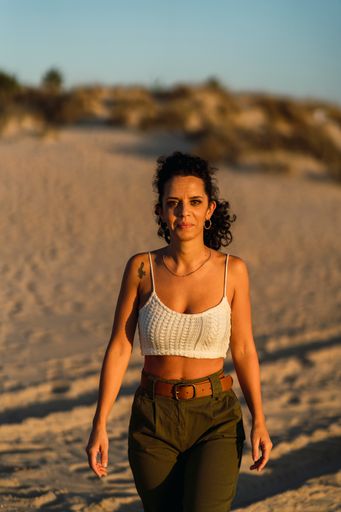 A vertical shot of a sexy young female with curly hair and a small tattoo posing on a sunny beach