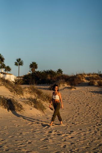 A vertical shot of a sexy young female with curly hair walking and posing on a sunny beach