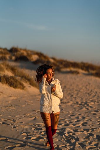 A vertical shot of an attractive female with tattooed and a cozy cardigan walking on a beach
