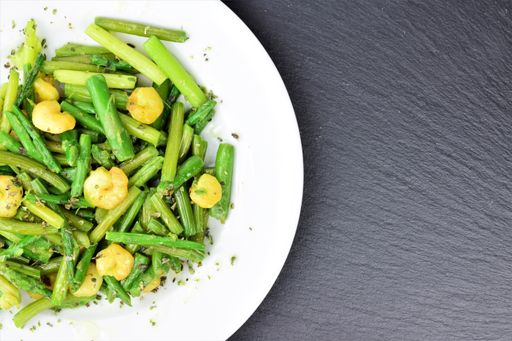 A top view of a plate of asparagus with prawns, spices, and olive oil on a black background with copy space