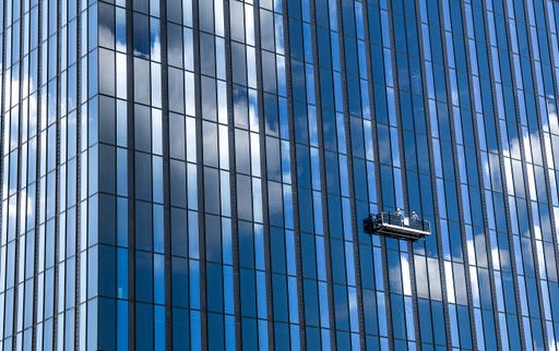 A tall skyscraper and professional high rise window cleaning service workers in a gondola