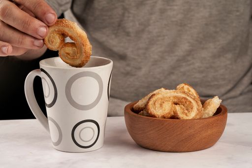 The man's hand dipping puff pastry palmeritas orejitas cup tea coffee