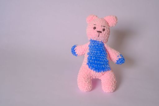 A handmade pink teddy bear with blue textured accents is displayed against a plain light backdrop.