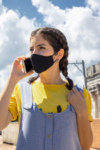 A Hispanic girl from Cuba in a black face mask talking on the phone outdoors