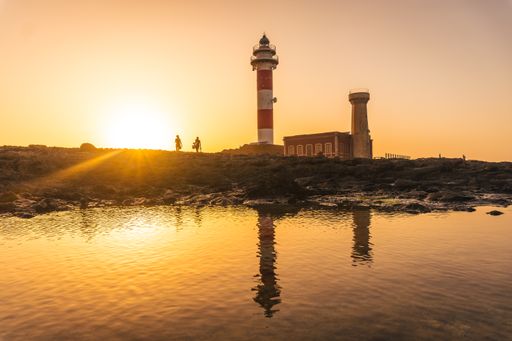 A silhouette of a couple next to the Toston Lighthouse at sunset in Punta Ballena, Fuerteventura, Canary Islands, Spain
