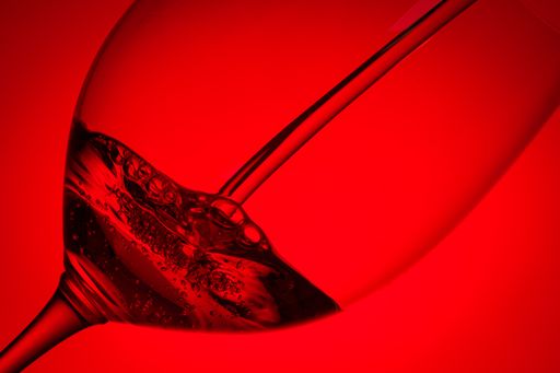 A closeup shot of wine pouring in a glass with bright red background