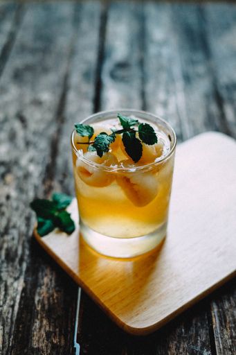 A vertical closeup shot of an alcoholic orange cocktail in a glass on a wooden coaster with a mint leaf on top