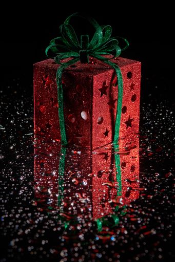 A vertical shot of a shiny gift box decoration on a mirror surface on a black background