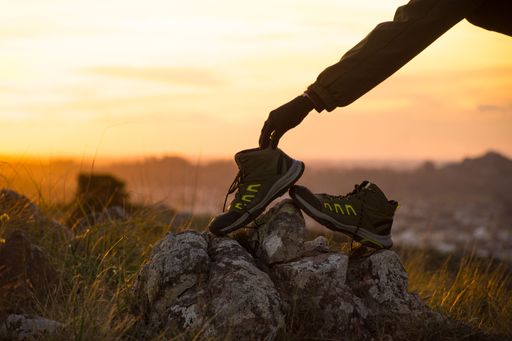 A person placing hiking boots on rocks during a golden sunset in a grassy field, highlighting outdoor adventure.