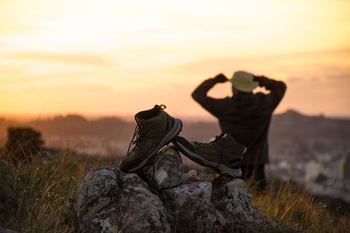 Hiking boots on rocks with a person in the background enjoying a sunset view in the mountains.
