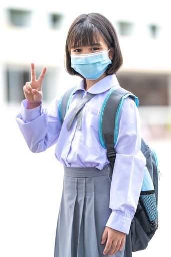 A cheerful Asian kid in a student uniform with a medical face mask during pandemic - back to school