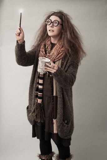 Vertical shot of a Caucasian girl with goofy glasses as a Trelawney wizard, Harry Potter character, with  tea cup in left hand and wand in right hand