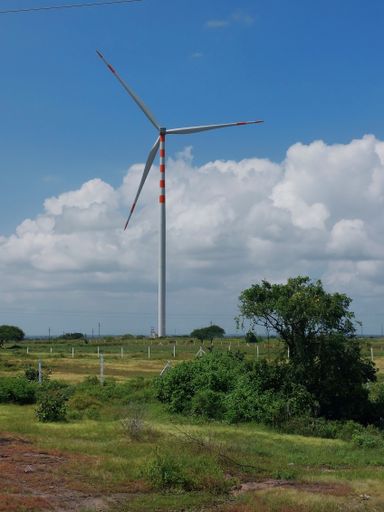 A vertical shot of a wind turbine in a beautiful green field under the partly cloudy sky