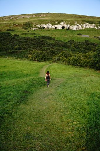 A vertical shot of a female hiking on the hill covered in greenery
