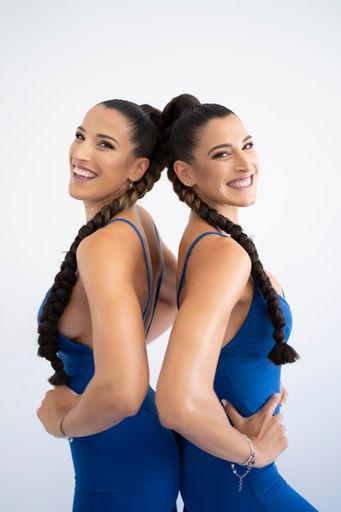 Two attractive Caucasian female friends wearing fitness outfits posing against a white wall