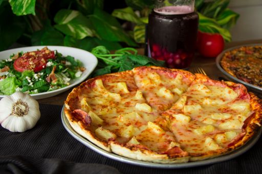 A closeup shot of a gourmet Hawaiian pizza and Italian salad bowl on the table