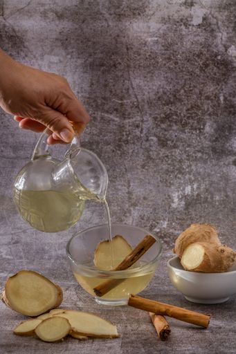 preparation of a ginger and cinnamon infusion with fresh produce natural roots and cinnamon stick served in a pitcher and a cup