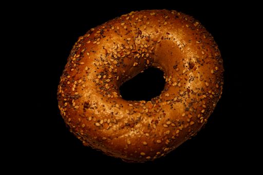 Close-up of a sesame seed bagel on a black background, highlighting texture and detail.