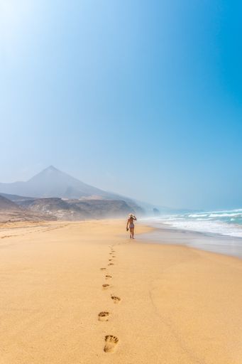 A back view of a young woman walking alone on the wild Cofete beach of the Jandia natural park, Spain