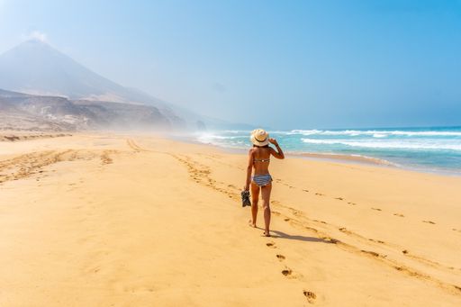 A back view of a young woman walking alone on the wild Cofete beach of the Jandia natural park, Spain