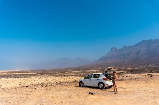 A young girl with the rental car on the Cofete beach of the Jandia natural park, Barlovento, south of Fuerteventura, Canary Islands, Spain