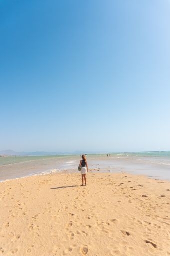 A back view of young Spanish woman walking along Sotavento beach, Fuerteventura, Canary Islands, Spain