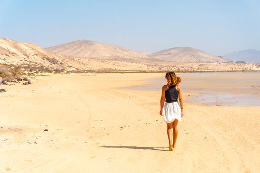 A back view of young Spanish woman walking along Sotavento beach, Fuerteventura, Canary Islands, Spain