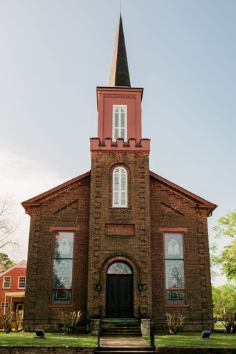 A historic brick church with tall steeple against a clear blue sky, showcasing Gothic architecture.