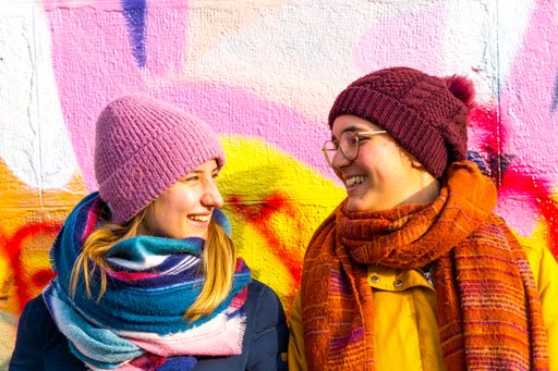 A shot of a happy lesbian Caucasian couple looking at each other in front of a colorful wall in Austria