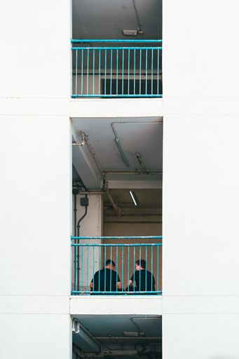 A vertical shot of two men talking on the balcony