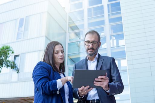 Businesswoman and businessman with tablet working in the street outside an office building, copy space