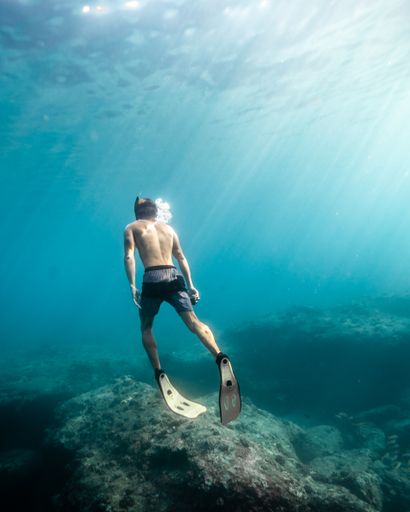 A vertical shot of a male swimming under water during a sunny day