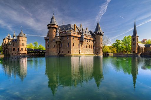 Stunning view of De Haar Castle reflecting in the tranquil waters under a vibrant blue sky.