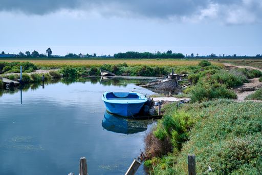 A river with a small boat surrounded by a field against a cloudy sky