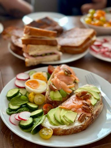 Delicious brunch with avocado toast, smoked salmon, pecans, and fresh vegetables on a white plate.