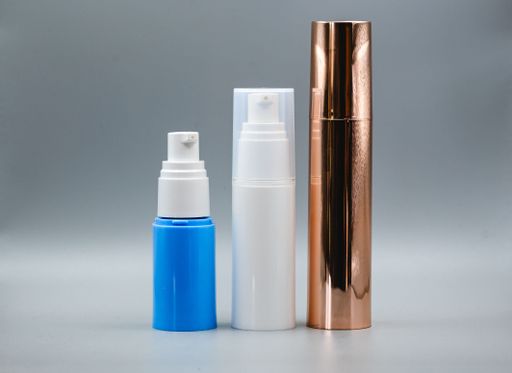 Three cosmetic bottles in different colors and sizes on a gray background.
