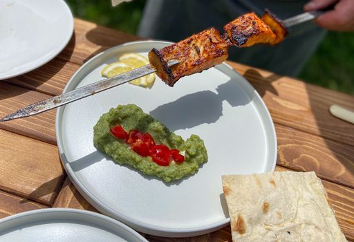 The grilled meat skewer over a plate with green mashed peas and tomatoes, served with lemon slices.