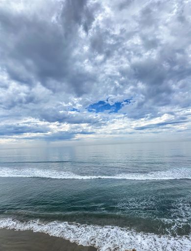 A vertical shot of a beautiful ocean with calm foamy waves under a blue cloudy sky